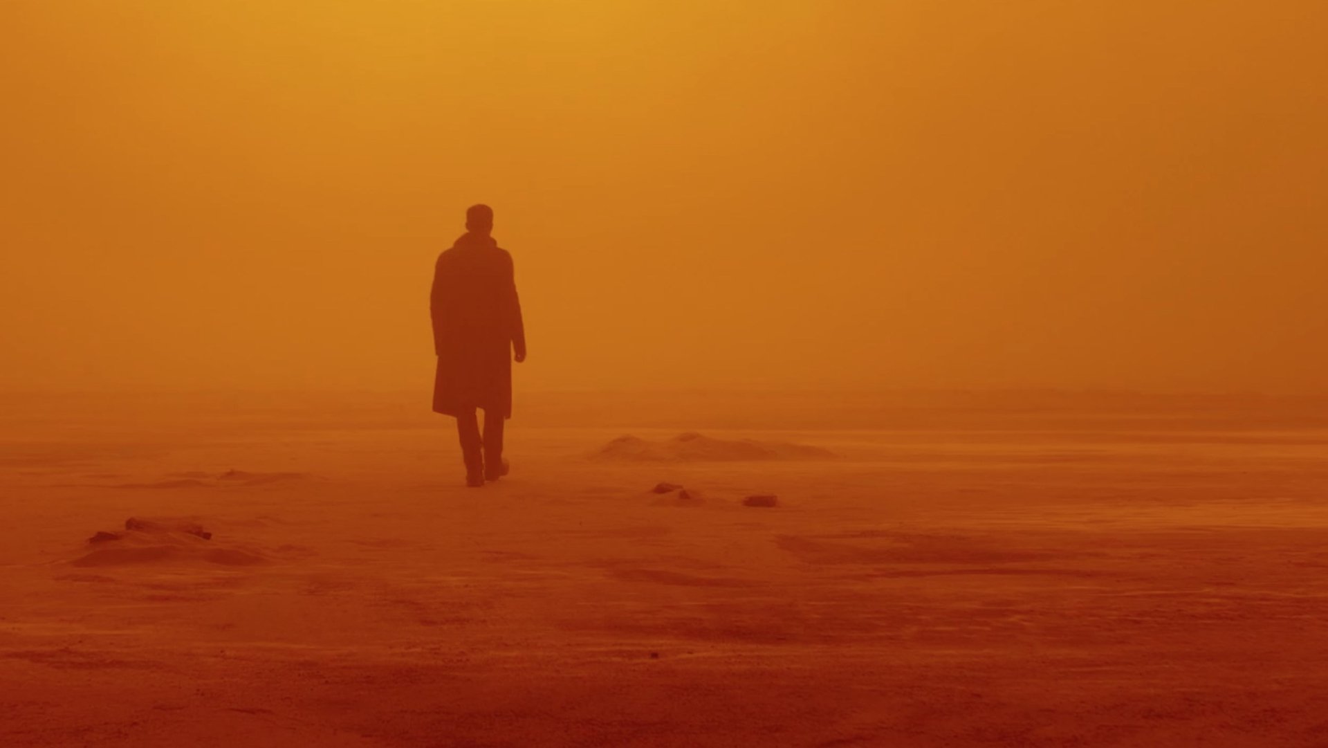 A silhueta de Ryan Gosling, em marrom, se distanciando de quem a olha enquanto se embrenha em um deserto com chão, céu e névoa amarelos